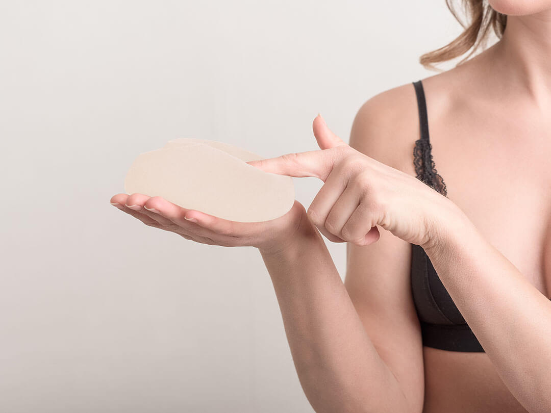 Young woman holding a breast implant before surgery